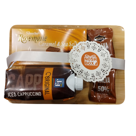 A gift package consisting of a bamboo board with a bar of Rosemarie caramel and sea salt chocolate, Achva halva, and a J&J iced cappuccino, wrapped in clear plastic, with a white ribbon and an orange sticker with the Nosh Box logo on a lace doily border.